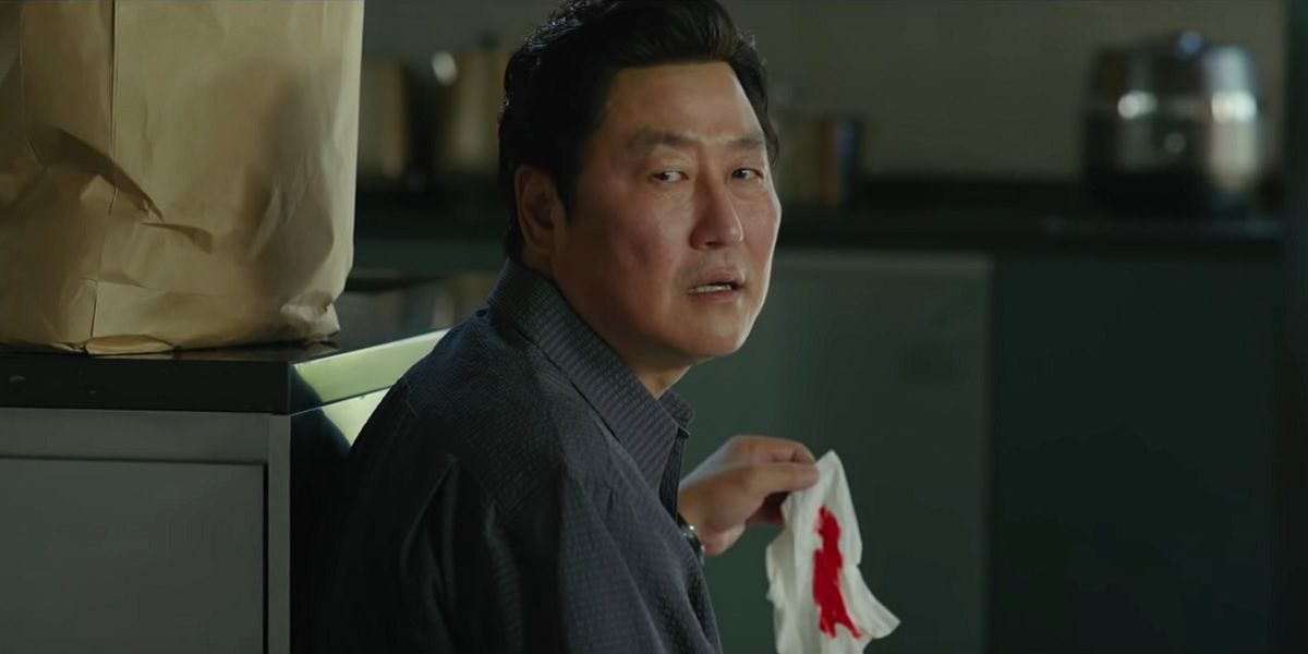 A man holds a bloody tissue and looks back at someone offscreen in Parasite.