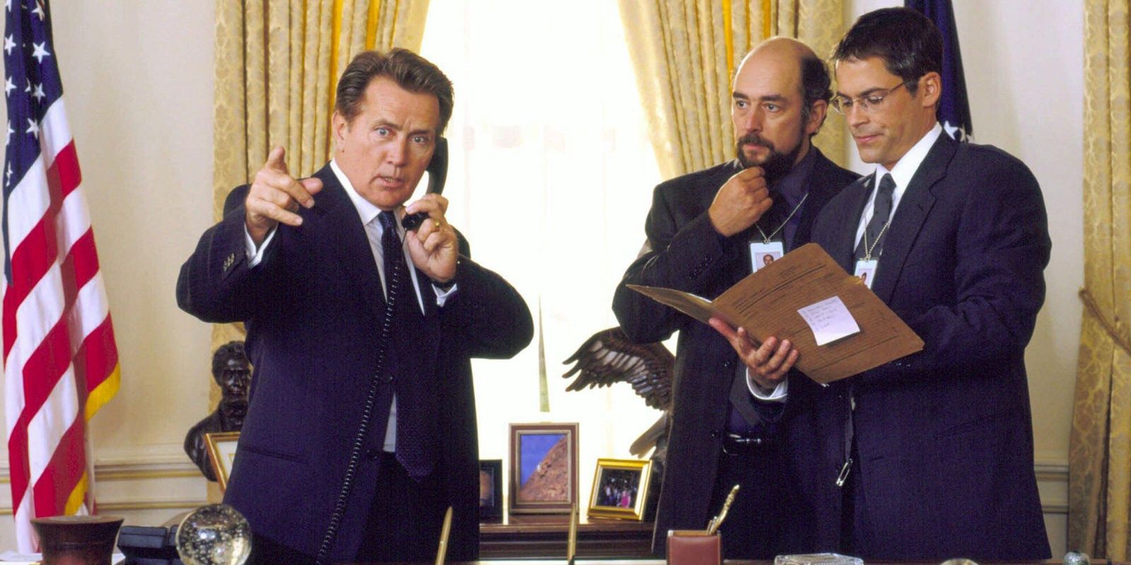 President Bartlet talks on the phone next to two staffers.