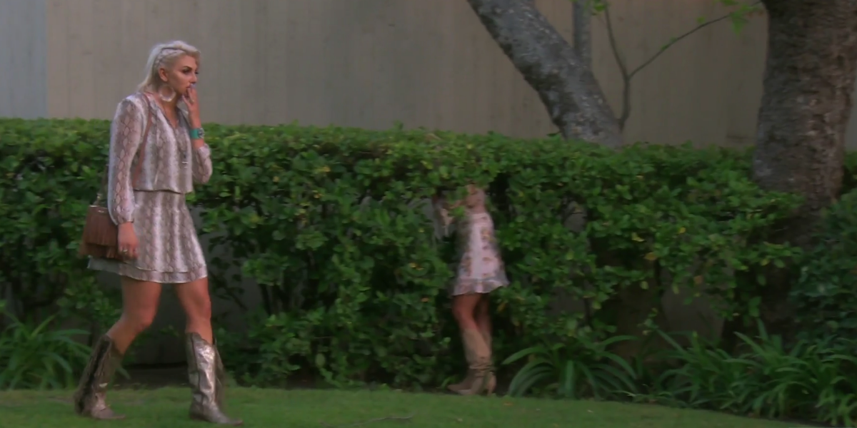 Gina walking past Tamra who has hid in a bush on RHOC