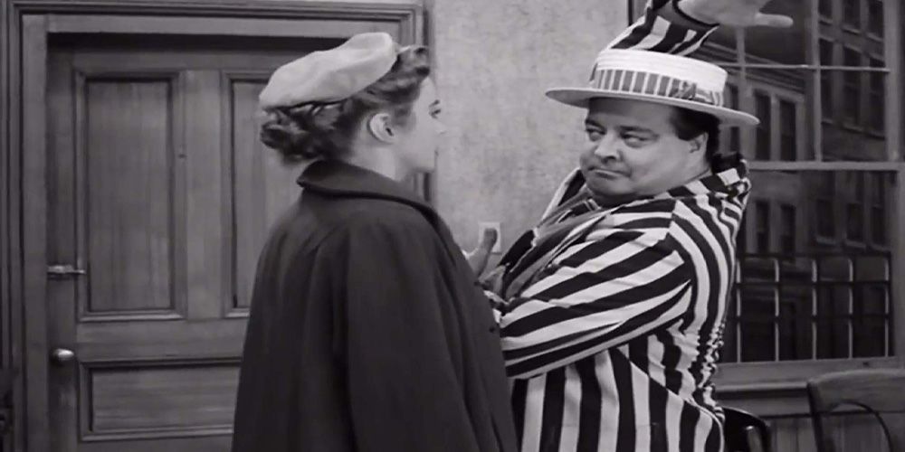 Ralph Kramden (Jackie Gleason), dressed as if in a barbershop quartet, does a dance move in front of his wife Alice (Audrey Meadows)