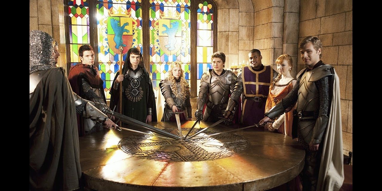 Image of all the main cast from Avalon High at a huge round table with swords.