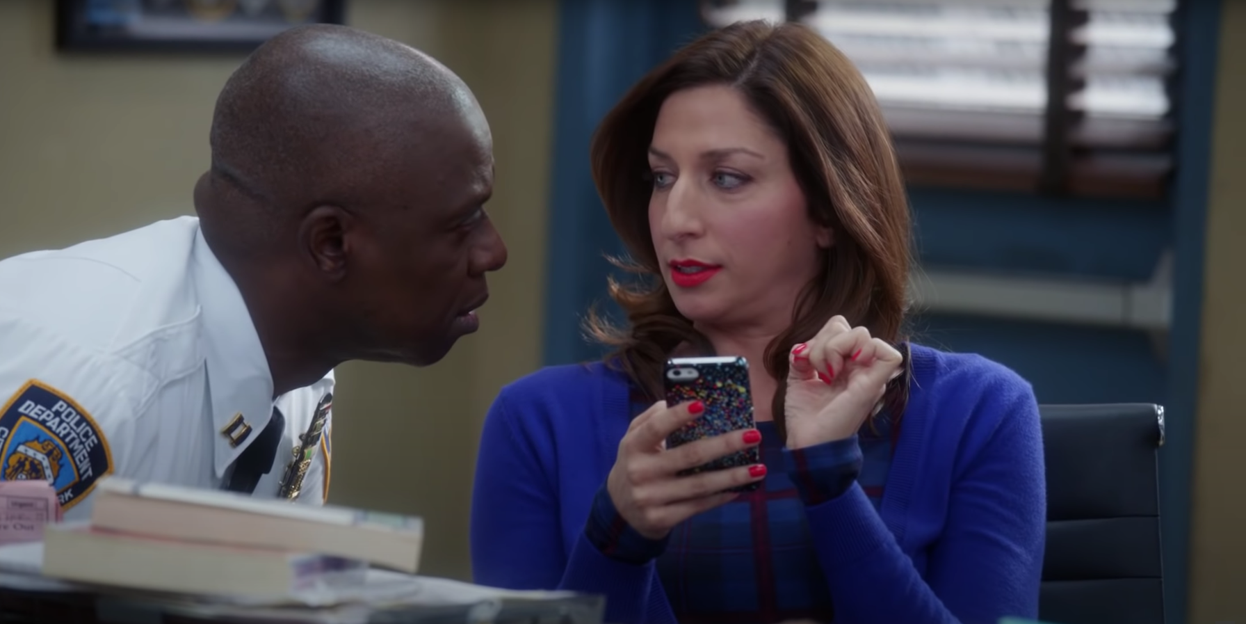 Holt leaning toward Gina while she is using her phone in Brooklyn Nine-Nine