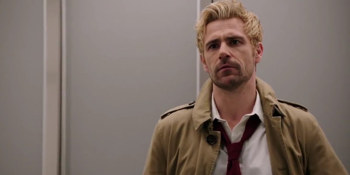 Constantine against a wall in a trench coat