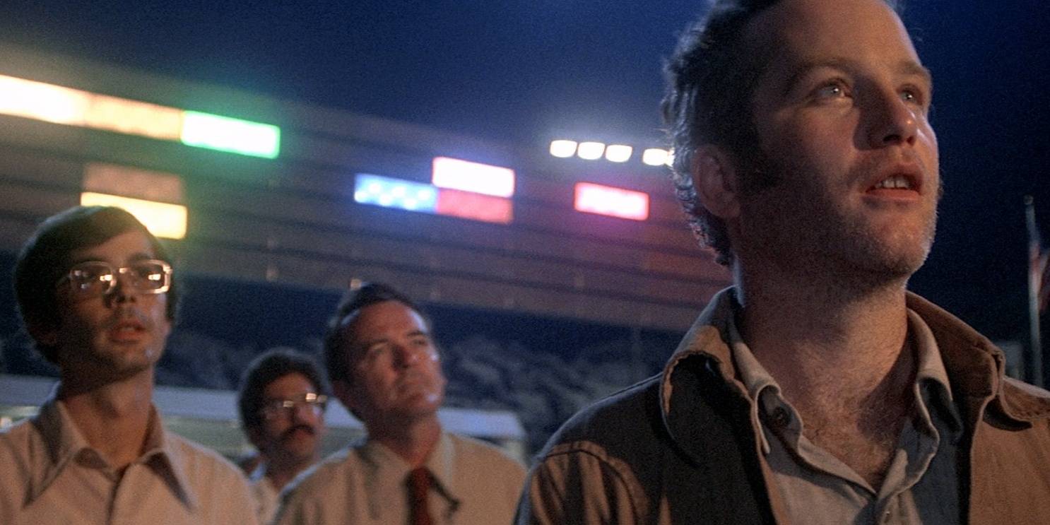 Richard Dreyfuss olhando para a nave alienígena com os cientistas e luzes atrás dele em Contatos Imediatos do Terceiro Grau