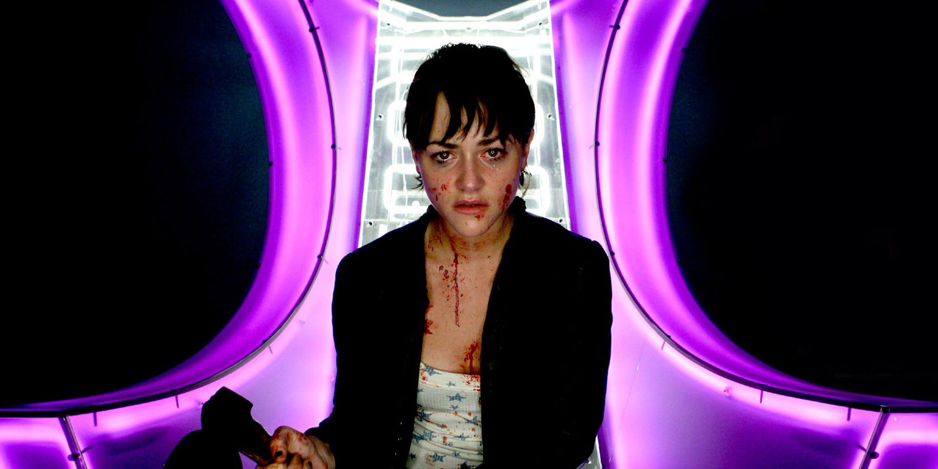 A woman sitting inside a room lit by purple lights in Dead Set