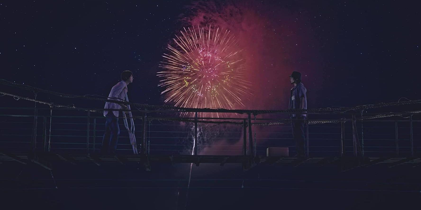 A firework explodes behind two people on a bridge