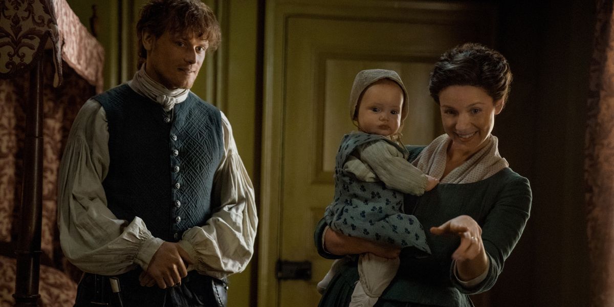 Claire holding Jemmie as Jamie stands near by in Outlander