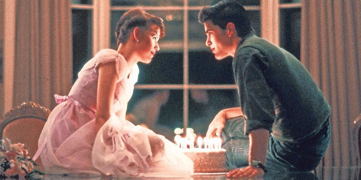 Sam and Jake sit on the table with her birthday cake in Sixteen Candles
