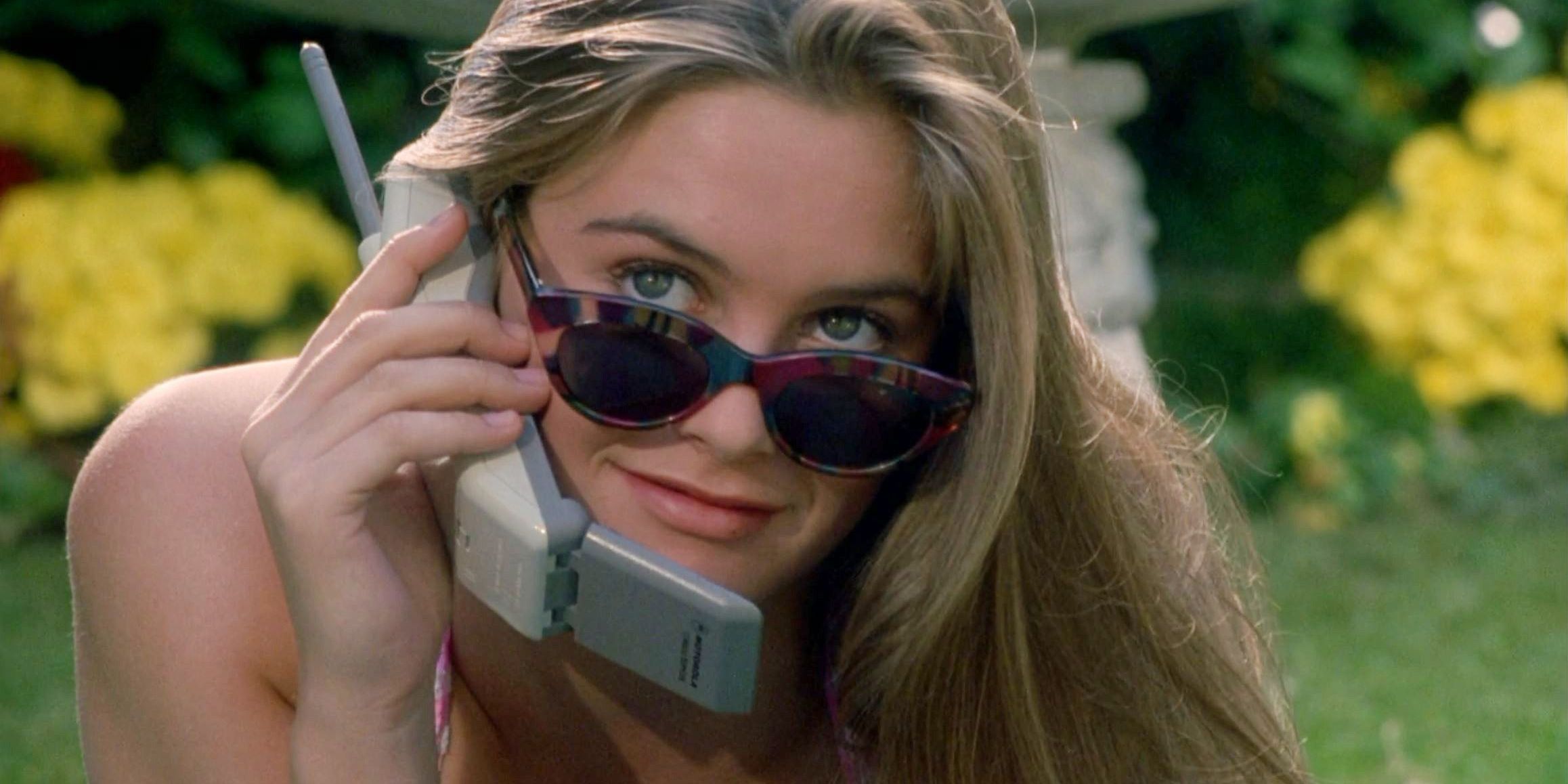 Alicia Silverstone ao telefone no jardim e olhando por cima dos óculos escuros em The Crush