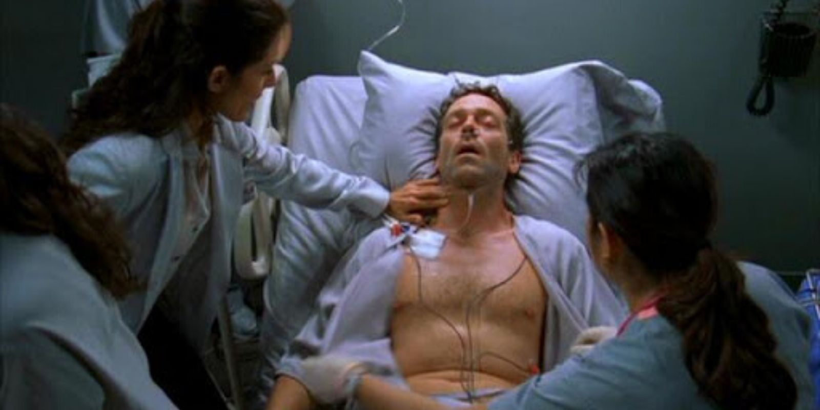 Hugh Laurie como Gregory House em uma cama de hospital com enfermeiras e médicos trabalhando nele em House, MD