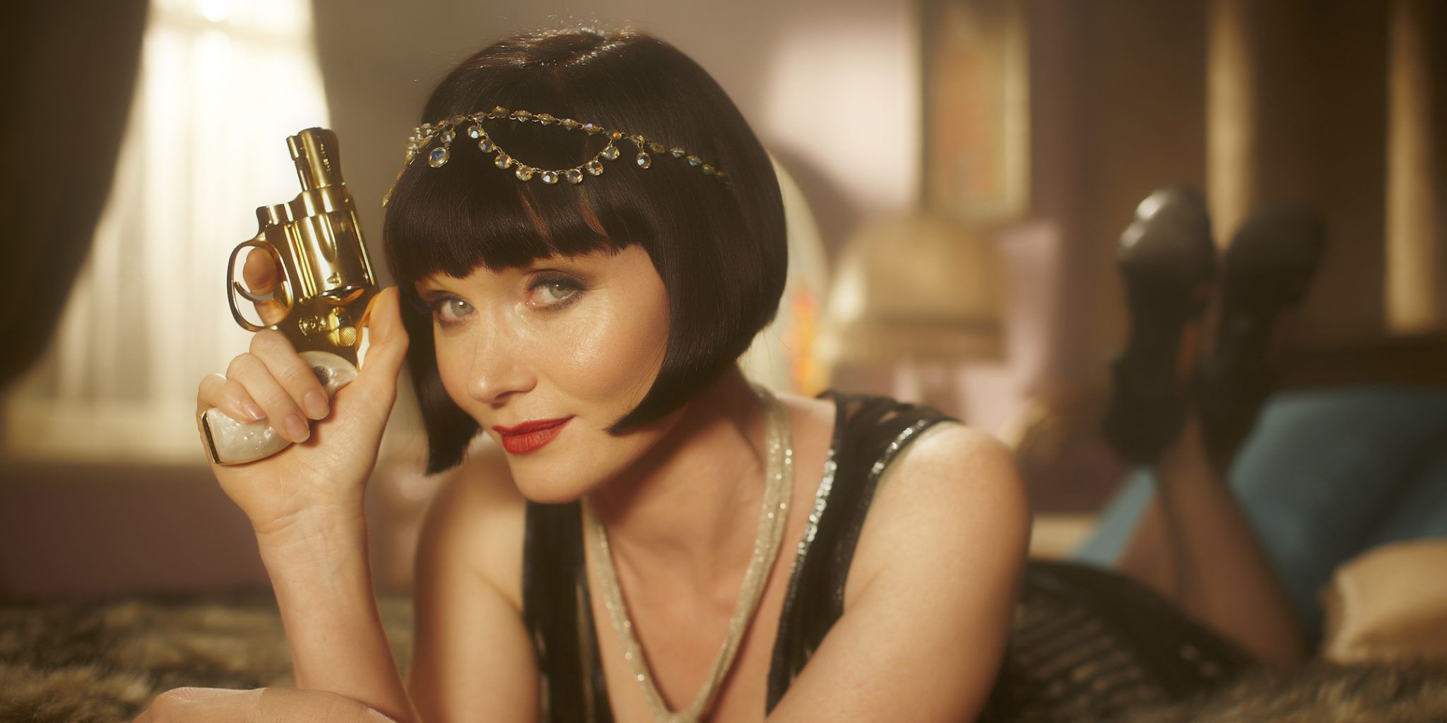 A young woman smiling while holding a golden gun in Miss Fisher's Murder Mysteries.