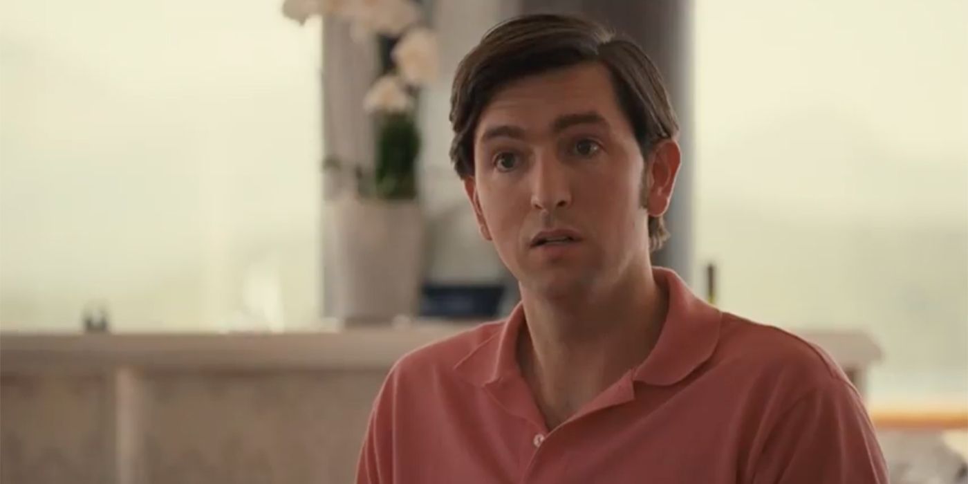 Succession's cousin Greg is wearing an orange polo shirt with a puzzled look on his face