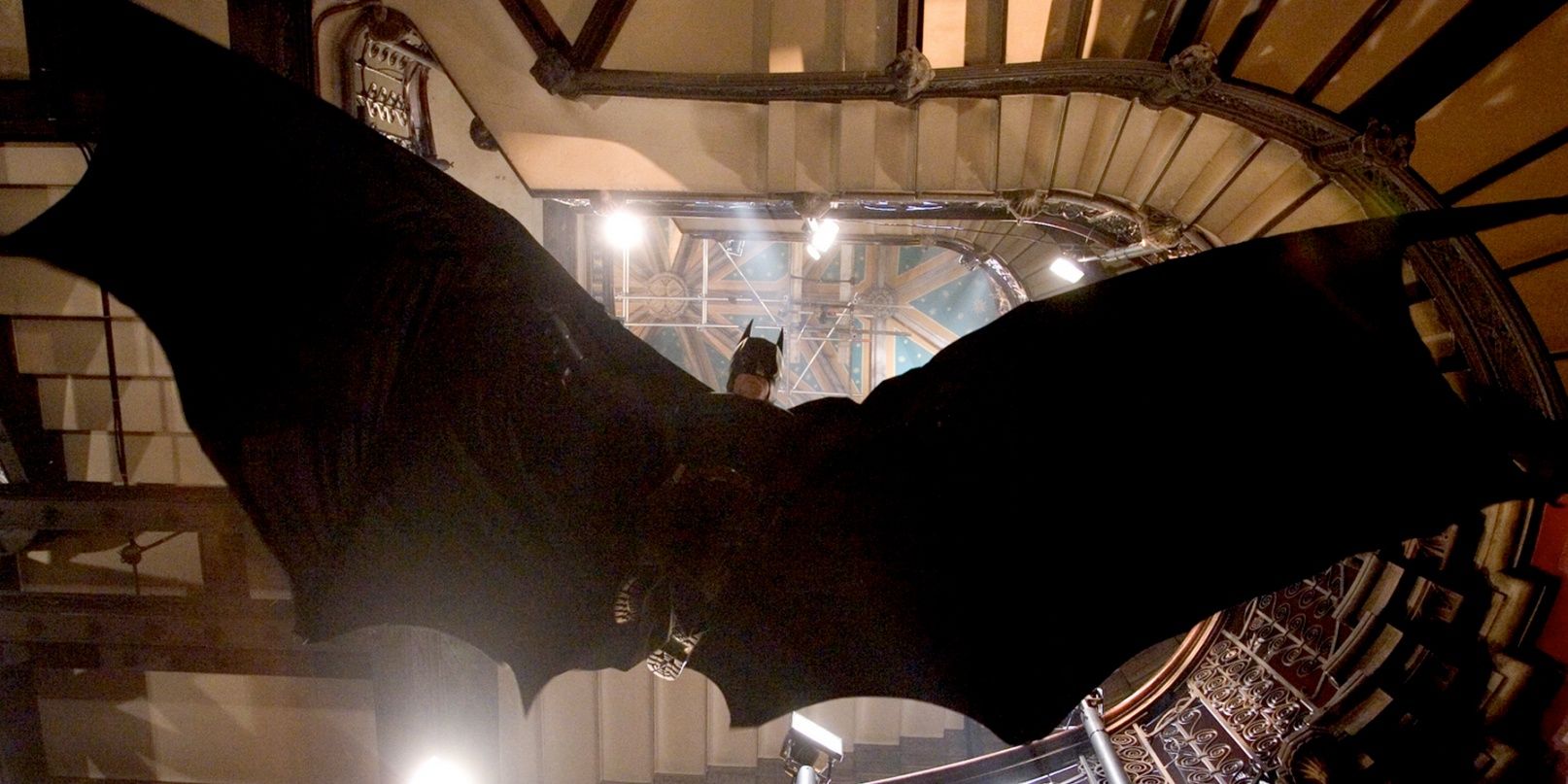 Batman soars down stairwell with his cape making the shape of a bat in Batman Begins