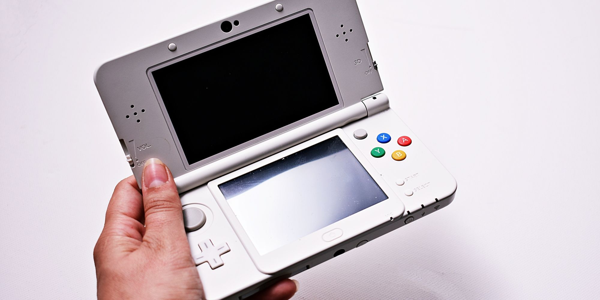 A person's left hand holding a Nintendo 3DS in front of a white background.
