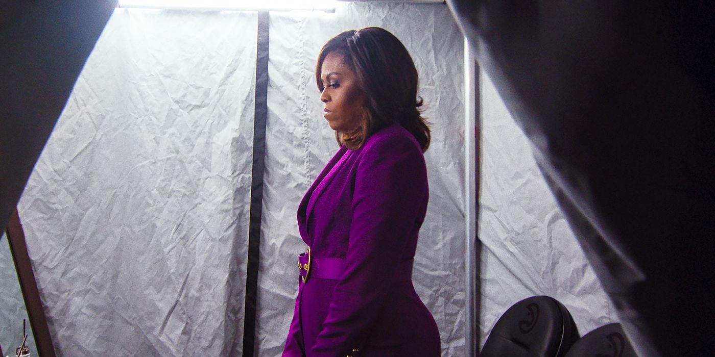 Michelle Obama de terno roxo de perfil lateral olhando para baixo e mal-humorada em Becoming Michelle Obama Netflix