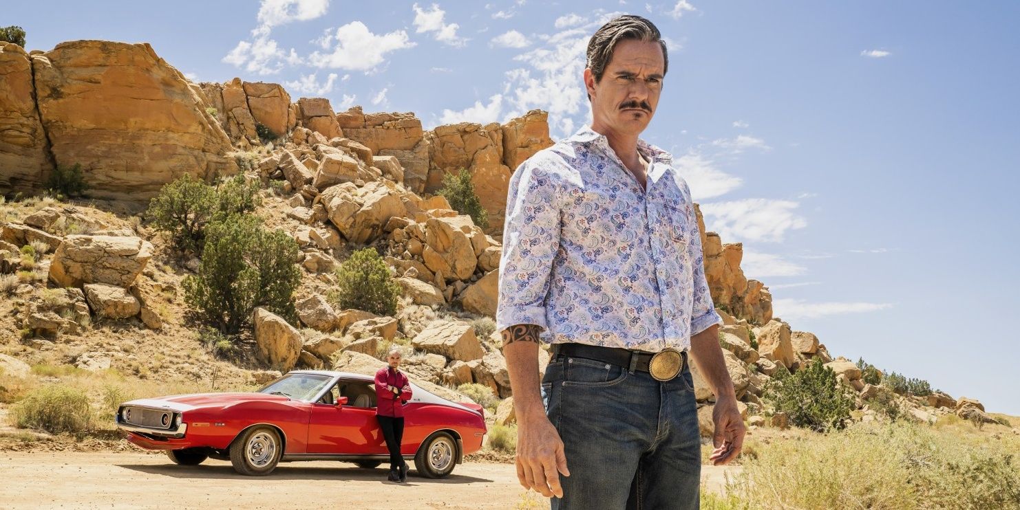 Lalo standing with a serious look on his face, with a red car behind him in Better Call Saul