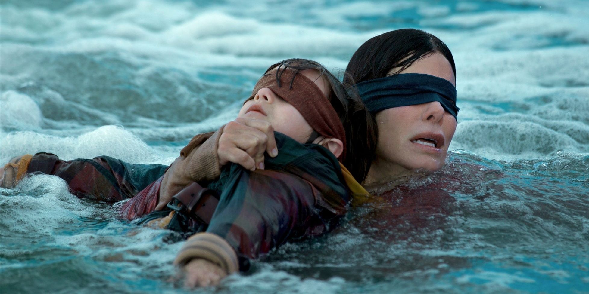 Sandra Bullock swimming blindfolded holding a child in Bird Box.