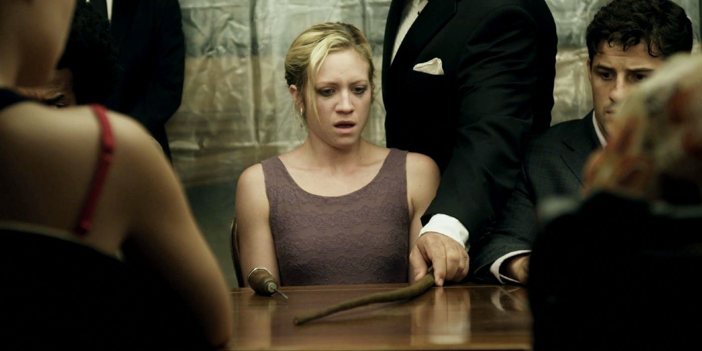 Brittany Snow appearing shocked at a table with others around her and tools in front of her In Would You Rather Movie