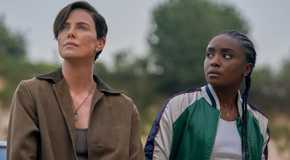 Charlize Theron and KiKi Layne look up at the sky while leaning against a car in The Old Guard