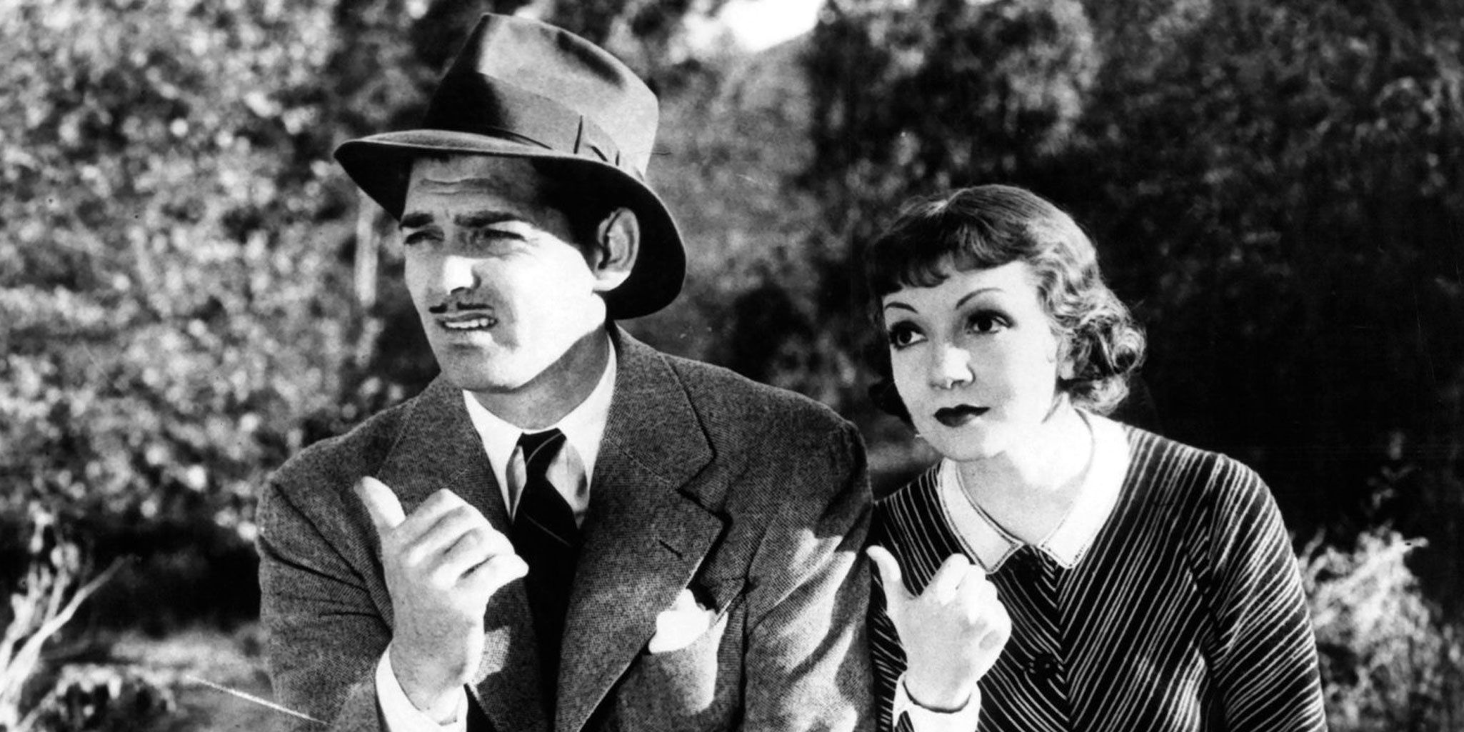 Clark Gable and Claudette Colbert sitting side by side and waiting for a ride on the road in It Happened One Night