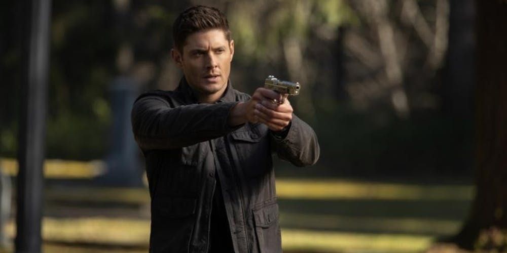 Dean points gun off camera in a park in Supernatural