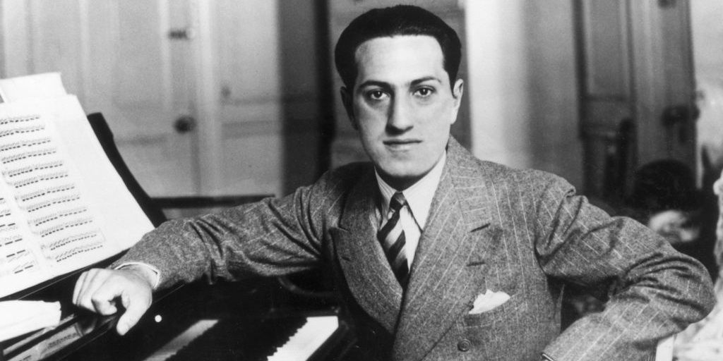 George Gershwin sits by a piano