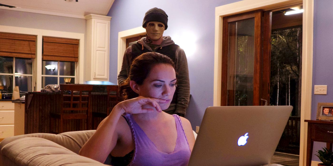 Maddie (Kate Siegel) at her laptop while an assailant approaches her from behind in Hush