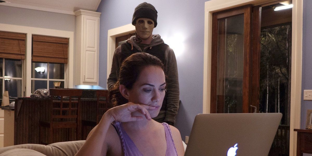 Maddie working on her computer with a masked man behind her in Hush