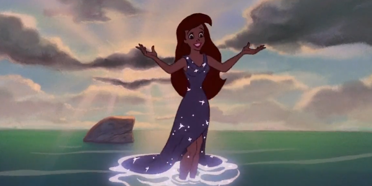 Ariel stands in the ocean while wearing a sparkly dress in the little mermaid