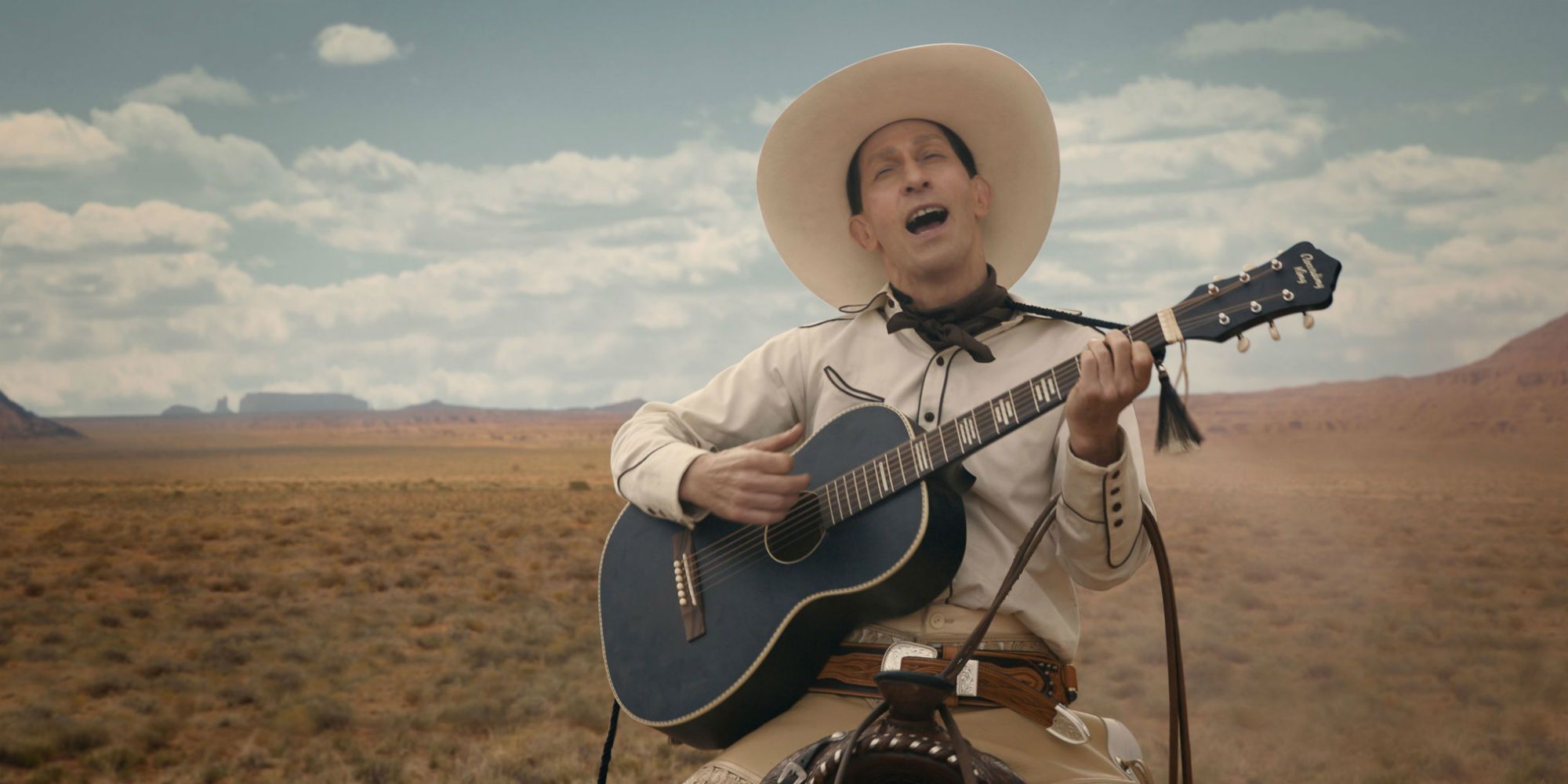 Tim Blake Nelson as Buster Scruggs playing his guitar and singing in the desert in The Ballad Of Buster Scruggs (2018)