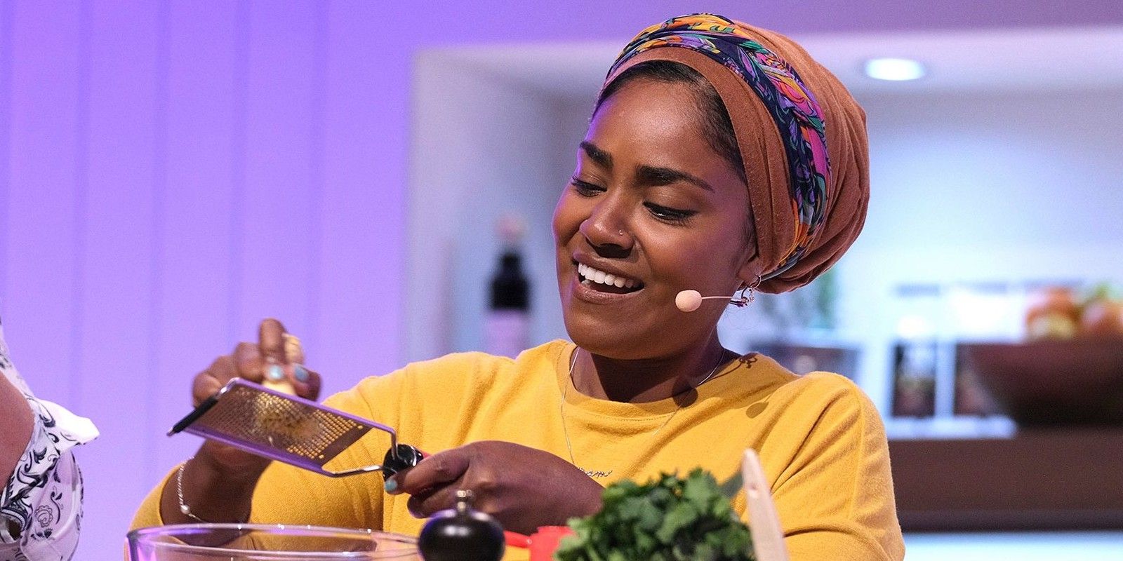 Nadiya Hussain in a yellow top and beige headgear cooking