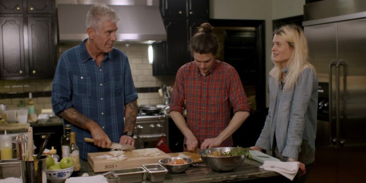Anthony Bourdain slicing ingredients on a kitchen counter with two people next to him in Parts Unknown.