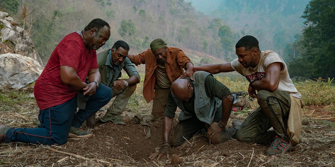 The main characters from Da 5 Bloods looking down at something on the ground.