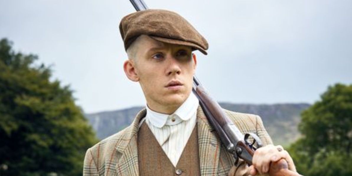 joe cole as john shelby in peaky blinders in a cap with a gun on his shoulders