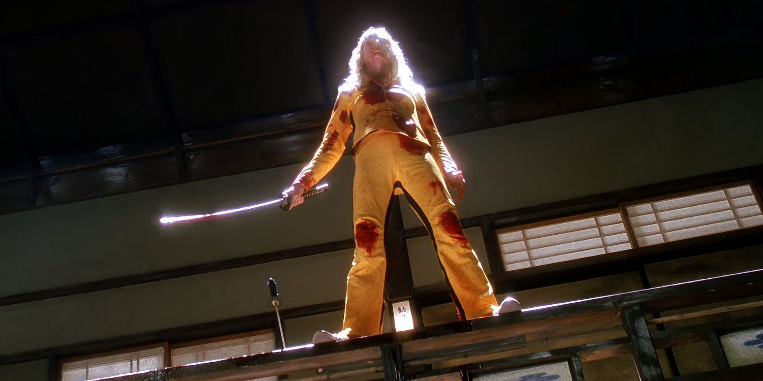 The Bride standing atop a bannister in her yellow suit and holding a sword in Kill Bill
