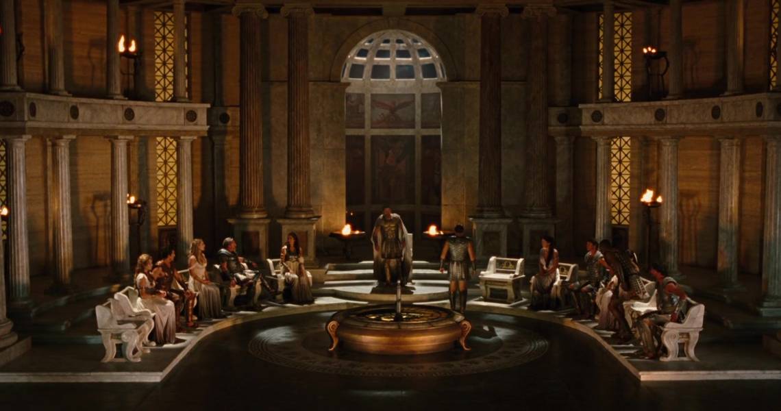 A still from the 20th Century Studio movie The Lightning Thief, where the Greek gods gather in a council, with Zeus in the center and Poseidon standing facing him.