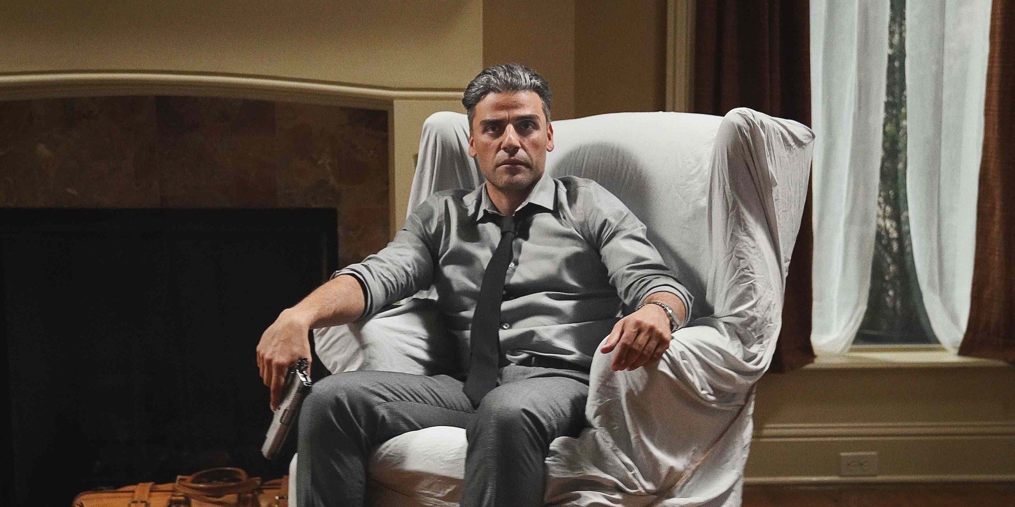 Oscar Isaac sits in a chair with a gun in The Card Counter