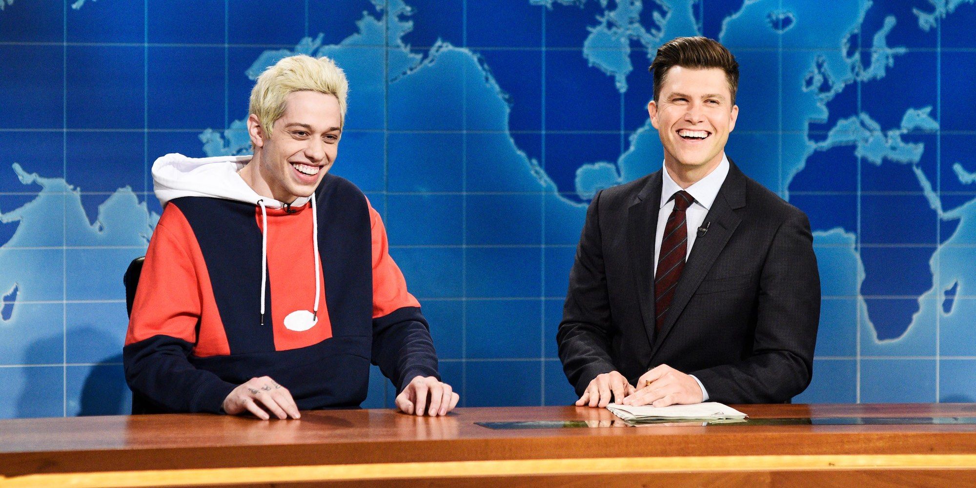 Pete Davidson and Colin Jost smiling in Weekend Update on Saturday Night Live