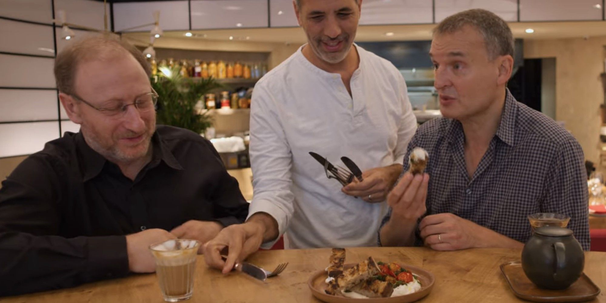 Phil Rosenthal e Yotam Ottolenghi comendo em uma mesa em Rovi em Somebody Feed Phil, temporada 3, episódio 3