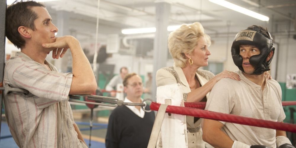 Melissa Leo pressing Mark Wahlberg's shouldes while Christian Bale stands against the ropes of a boxing ring in The Fighter
