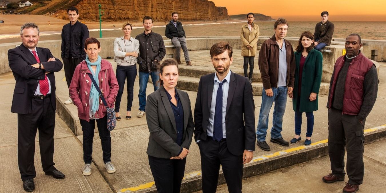 Over a dozen people stand outside near a beach in Broadchurch.