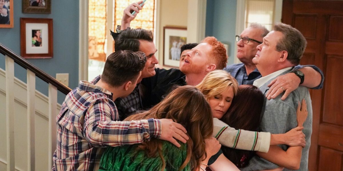 The cast of Modern Family hugging in the finale while Mitchell looks at his phone
