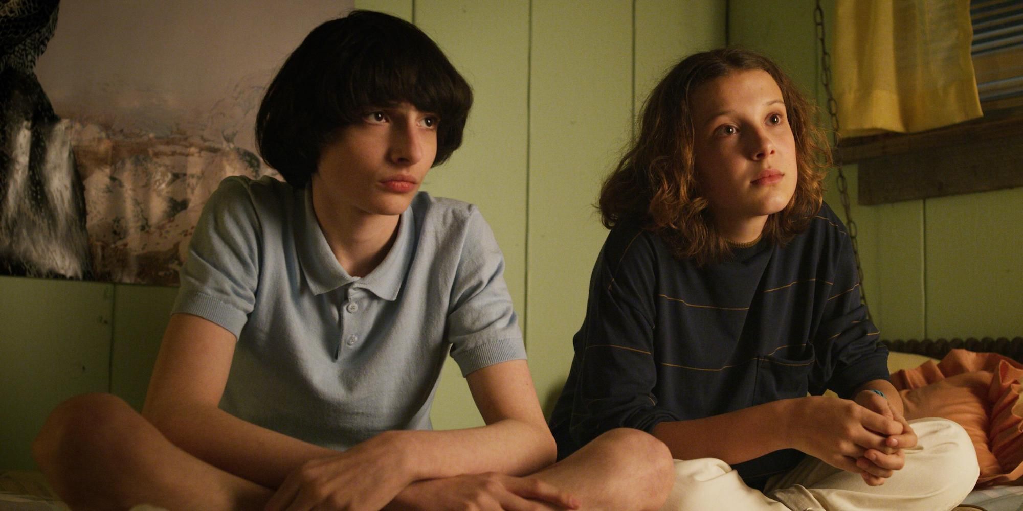 Mike and Eleven sitting on a bed in Stranger Things