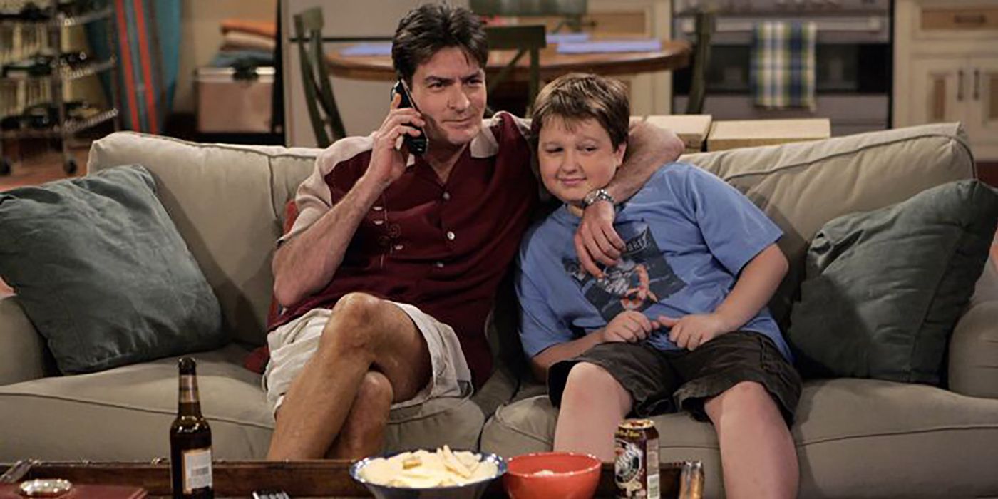 Charlie in a maroon bowling shirt hugging Jake on a couch in Two and a Half Men