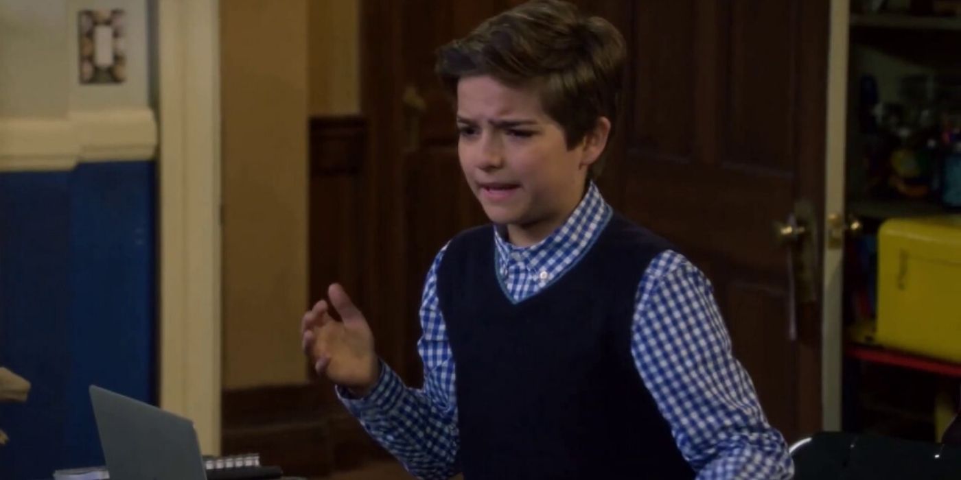 Max from Fuller House wearing a button shirt and vest with his hand up.