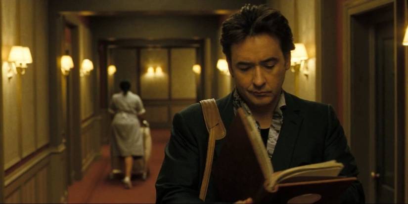 Mike reading a book while walking down a hallway in 1408