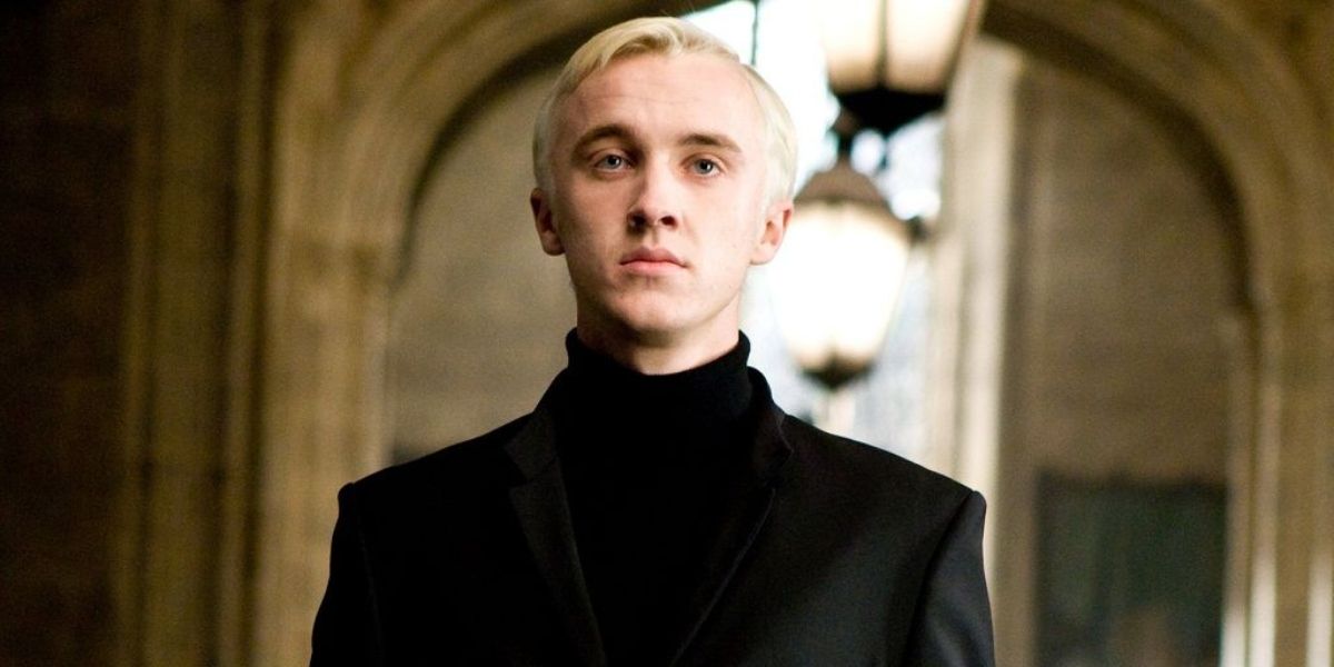 Draco Malfoy wearing a black suit and looking serious at Hogwarts