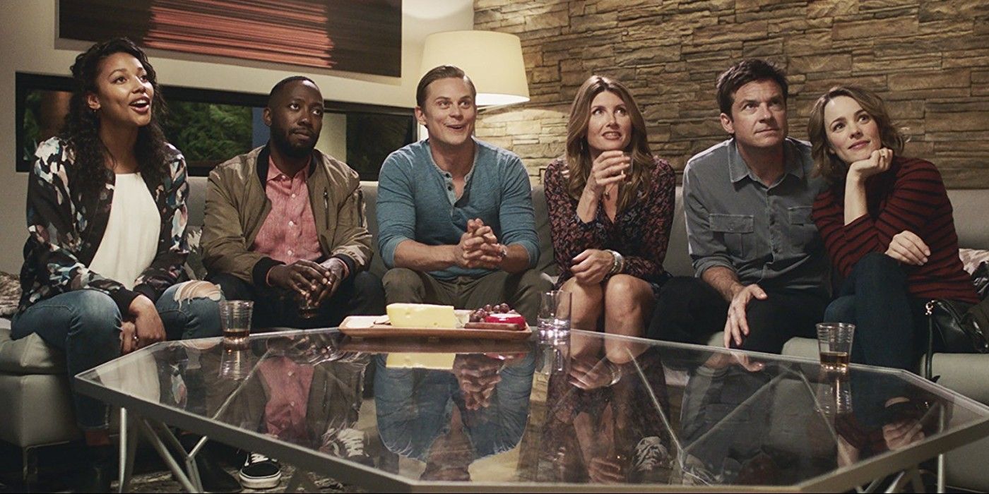 Um grupo de amigos sorrindo e se reunindo no sofá na Game Night