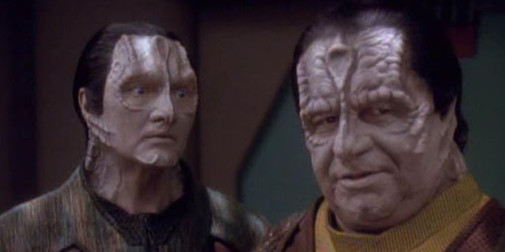 Two Romulans in DS9. One looks towards other who is looking at the camera