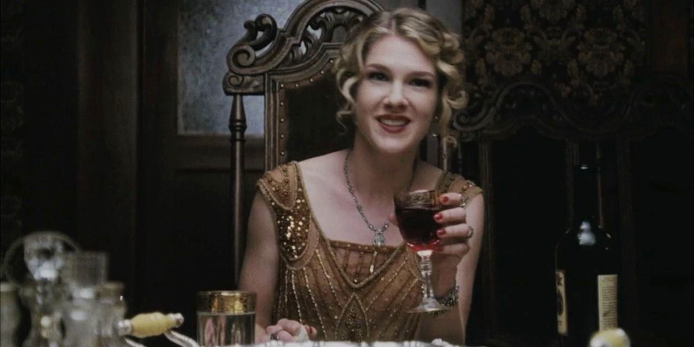 Nora Montgomery holding a glass of wine at the table in American Horror Story